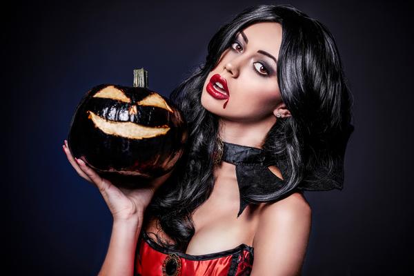 A sexy vampire stands with a Halloween pumpkin