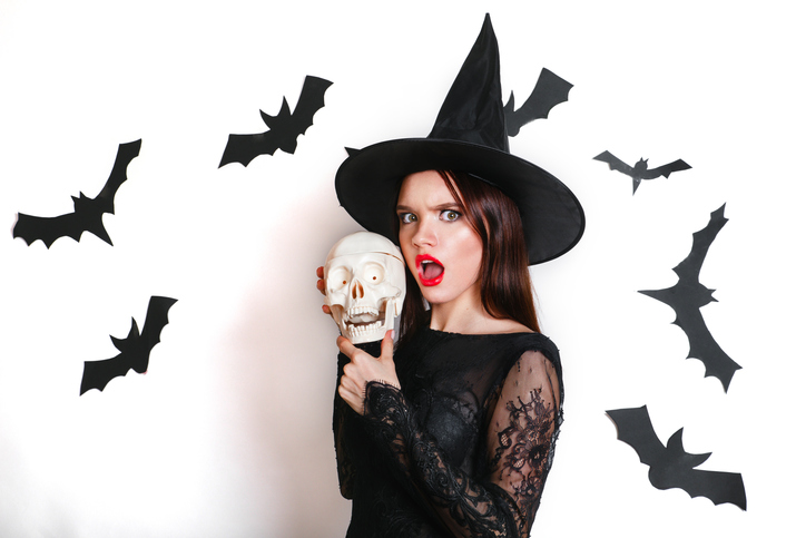sexy gothic young woman in witch halloween costume with hat standing and having fun over white background