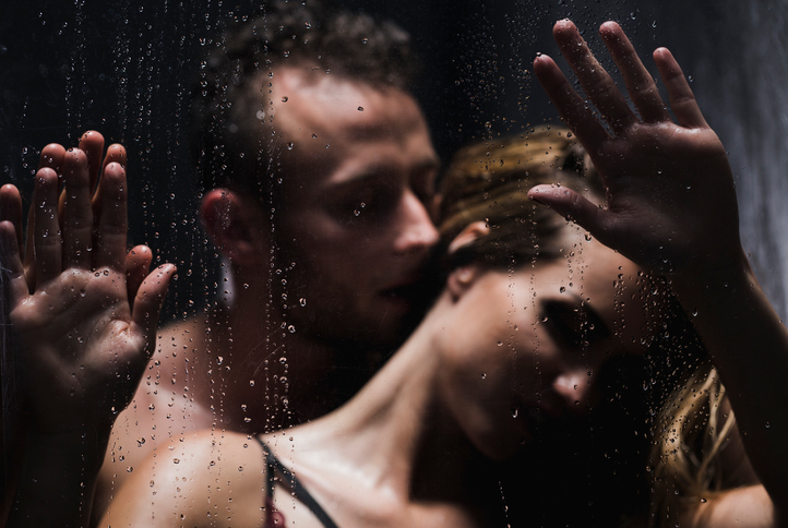 Man whispering to woman's ear with his hands on glass shower during foreplay