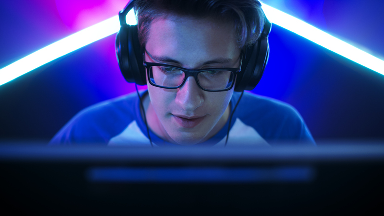 Professional Gamer Plays in MMORPG/ Strategy/ Shooter Video Game on His Computer. He's Participating in Online Cyber Games Tournament, Plays at Home, or in Internet Cafe. He Wears Glasses and Gaming Headphones, Talks into Microphone.