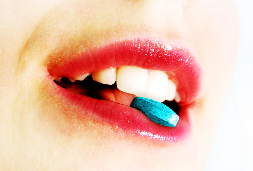 Woman biting on a blue viagra pill