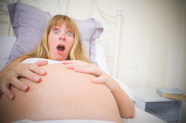 Woman looking shocked at her pregnant belly