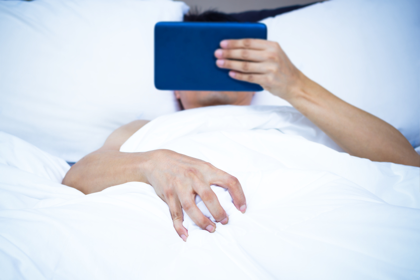 Young asian man lying on white bed & watching pornography on computer tablet. focus to right hand